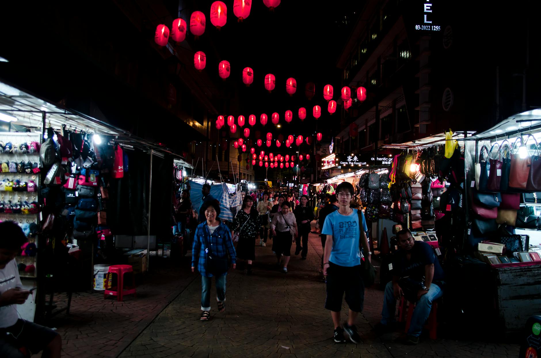Bustling night market street scene with colorful Asian lanterns illuminating food stalls and shoppers in Kuala Lumpur Malaysia