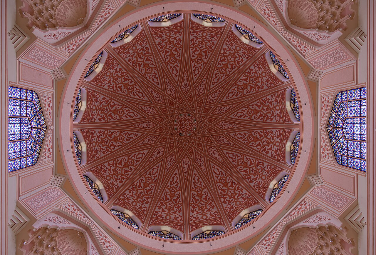 The pink and cream interior dome of Putra Mosque in Putrajaya, seen from directly below